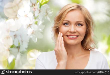 beauty, people and skincare concept - smiling woman in white shirt touching face over natural spring cherry blossom background