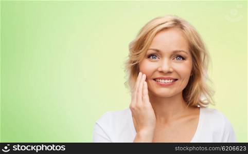 beauty, people and skincare concept - smiling woman in white shirt touching face over green natural background