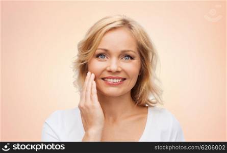 beauty, people and skincare concept - smiling woman in white shirt touching face over beige background