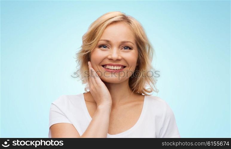 beauty, people and skincare concept - smiling woman in white shirt touching face over blue background