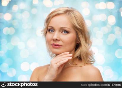 beauty, people and skincare concept - smiling woman with bare shoulders touching face over blue holidays lights background