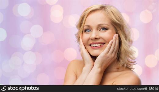 beauty, people and skincare concept - smiling woman with bare shoulders touching face over pink lights background