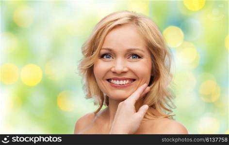 beauty, people and skincare concept - smiling woman with bare shoulders touching face over green summer lights background