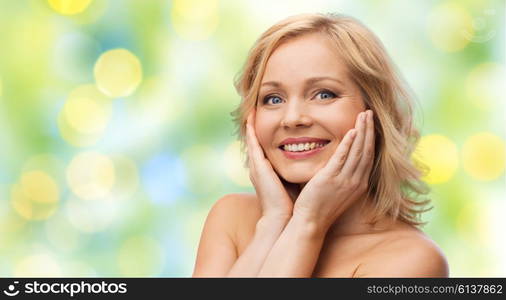 beauty, people and skincare concept - smiling woman with bare shoulders touching face over green summer lights background