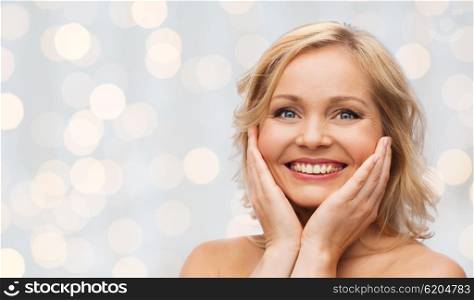beauty, people and skincare concept - smiling woman with bare shoulders touching face over holidays lights background