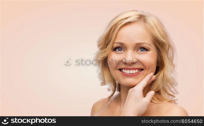 beauty, people and skincare concept - smiling woman with bare shoulders touching face over beige background