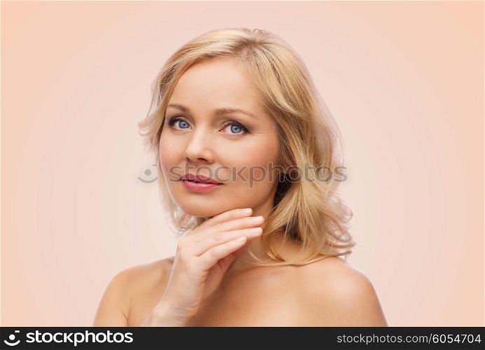 beauty, people and skincare concept - smiling woman with bare shoulders touching face over beige background
