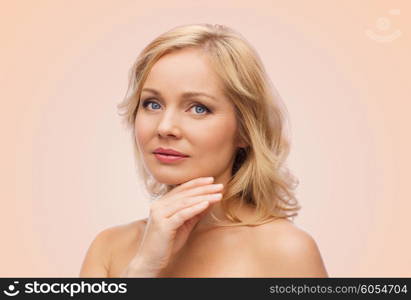 beauty, people and skincare concept - smiling woman with bare shoulders touching face over beige background