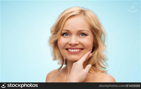 beauty, people and skincare concept - smiling woman with bare shoulders touching face over blue background