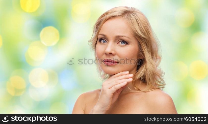beauty, people and skincare concept - woman with bare shoulders touching face over green summer lights background