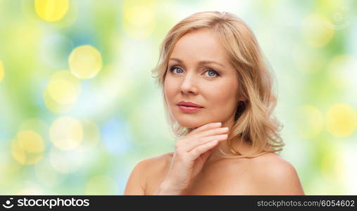 beauty, people and skincare concept - woman with bare shoulders touching face over green summer lights background