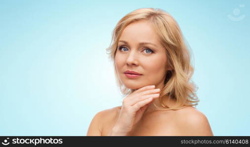 beauty, people and skincare concept - woman with bare shoulders touching face over blue background