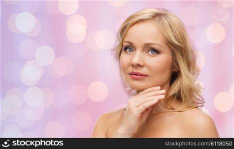 beauty, people and skincare concept - woman with bare shoulders touching face over pink lights background