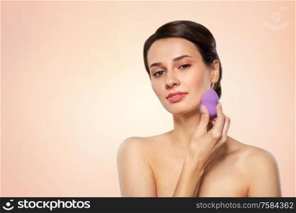 beauty, people and skincare concept - young woman applying foundation with make up blending sponge over beige background. young woman with sponge applying makeup