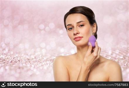 beauty, people and skincare concept - young woman applying foundation with make up blending sponge over shimmering pink glitter on background. young woman with sponge applying makeup