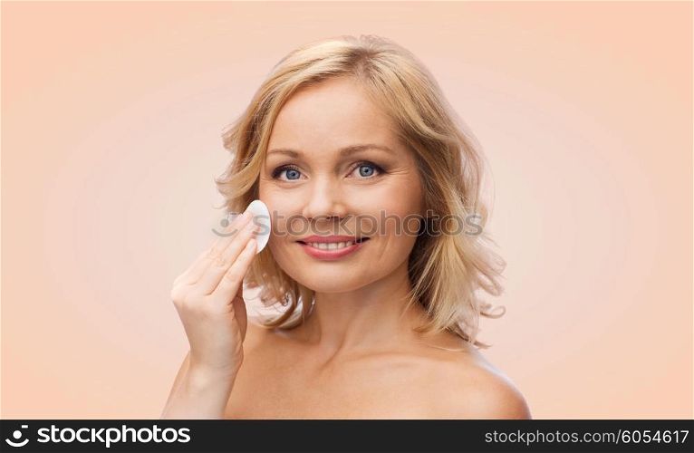 beauty, people and skincare concept - young woman cleaning face and removing make up with cotton pad over beige background