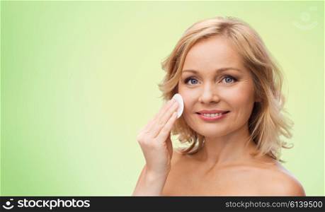 beauty, people and skincare concept - young woman cleaning face and removing make up with cotton pad over green natural background