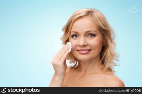 beauty, people and skincare concept - young woman cleaning face and removing make up with cotton pad over blue background