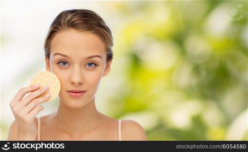 beauty, people and skincare concept - young woman cleaning face with exfoliating sponge over green natural background