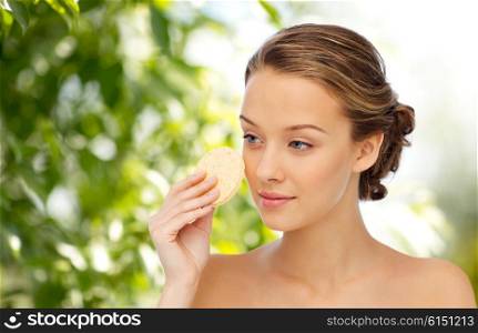 beauty, people and skincare concept - young woman cleaning face with exfoliating sponge over green natural background