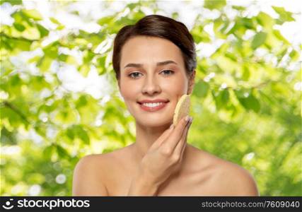beauty, people and skincare concept - young woman cleaning face with exfoliating sponge over green natural background. young woman cleaning face with exfoliating sponge