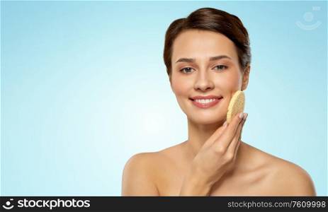 beauty, people and skincare concept - young woman cleaning face with exfoliating sponge over blue background. young woman cleaning face with exfoliating sponge