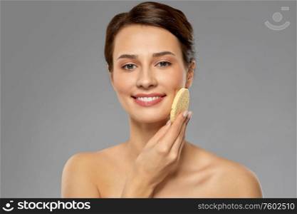 beauty, people and skincare concept - young woman cleaning face with exfoliating sponge over grey background. young woman cleaning face with exfoliating sponge