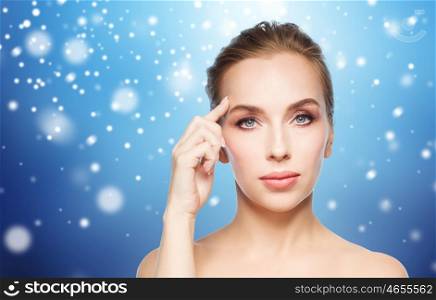 beauty, people and winter concept - beautiful young woman showing her forehead over blue background and snow