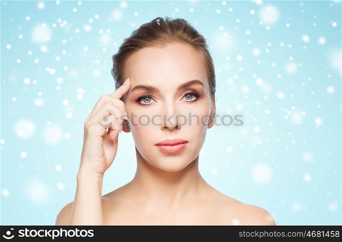 beauty, people and winter concept - beautiful young woman showing her forehead over blue background and snow
