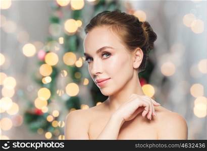 beauty, people and winter holidays concept - beautiful young woman face over christmas tree lights background