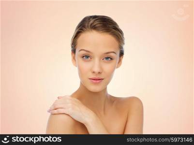 beauty, people, body care and health concept - smiling young woman face and hand on bare shoulder over beige background