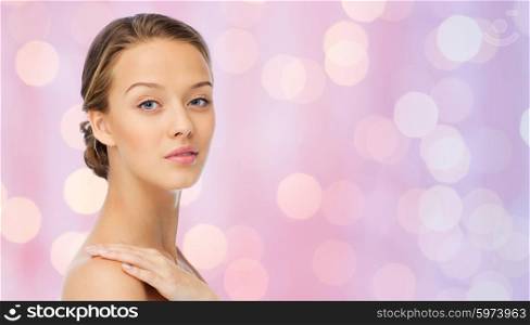 beauty, people, body care and health concept - smiling young woman face and hand on bare shoulder over pink lights background