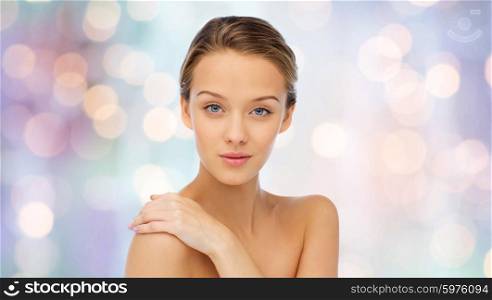 beauty, people, body care and health concept - smiling young woman face and hand on bare shoulder over purple holidays lights background
