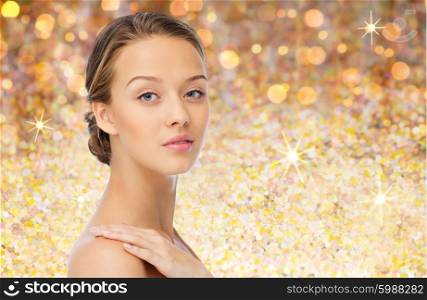 beauty, people, body care and health concept - smiling young woman face and hand on bare shoulder over golden glitter background