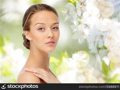 beauty, people, body care and health concept - smiling young woman face and hand on bare shoulder over green natural cherry blossom background