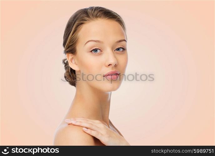 beauty, people, body care and health concept - smiling young woman face and hand on bare shoulder over beige background
