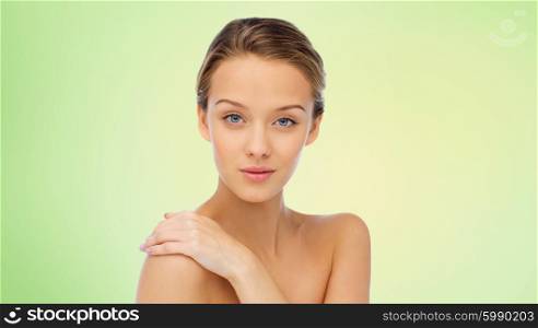 beauty, people, body care and health concept - smiling young woman face and hand on bare shoulder over green background