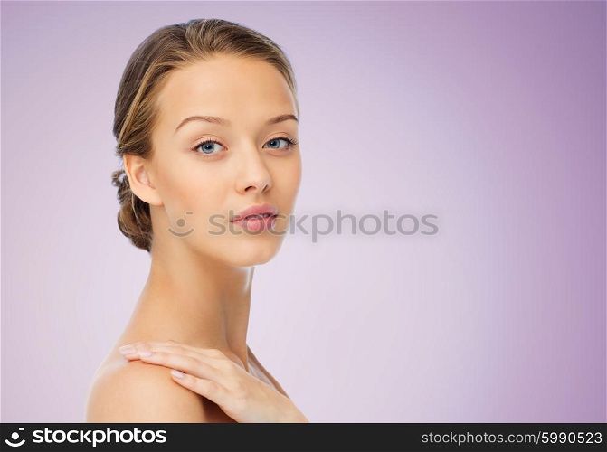 beauty, people, body care and health concept - smiling young woman face and hand on bare shoulder over violet background
