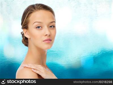 beauty, people, body care and health concept - smiling young woman face and hand on bare shoulder over blue water background