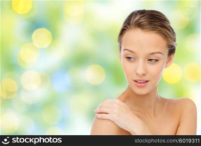 beauty, people, body care and health concept - smiling young woman face and hand on bare shoulder over green lights background