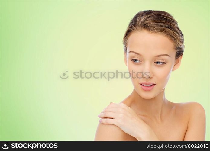 beauty, people, body care and health concept - smiling young woman face and hand on bare shoulder over green natural background