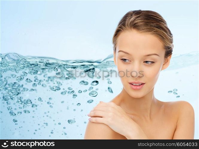 beauty, people, body care and health concept - smiling young woman face and hand on bare shoulder over water splash on blue background