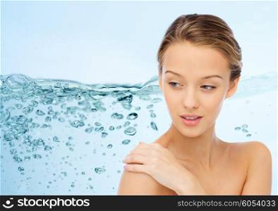 beauty, people, body care and health concept - smiling young woman face and hand on bare shoulder over water splash on blue background