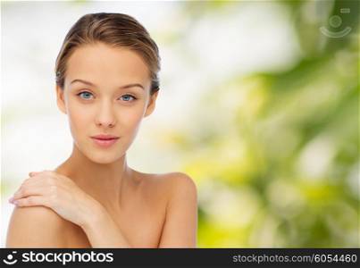 beauty, people, body care and health concept - smiling young woman face and hand on bare shoulder over green natural background