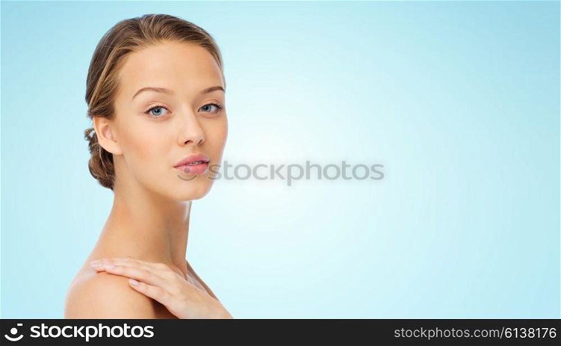 beauty, people, body care and health concept - smiling young woman face and hand on bare shoulder over blue background
