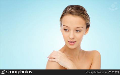 beauty, people, body care and health concept - smiling young woman face and hand on bare shoulder over blue background