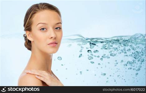 beauty, people, body care, moisturizing and health concept - smiling young woman face and hand on bare shoulder over water splash background