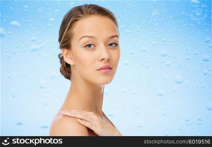 beauty, people, body care, moisturizing and health concept - smiling young woman face and hand on bare shoulder over water drops on blue background