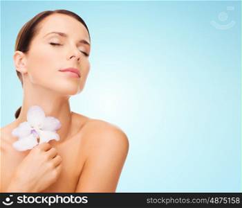 beauty, people, bodycare and health concept - beautiful young woman with orchid flower and bare shoulders over blue background