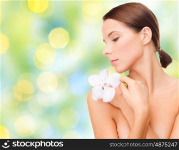 beauty, people, bodycare and health concept - beautiful young woman with orchid flower and bare shoulders over summer green lights background